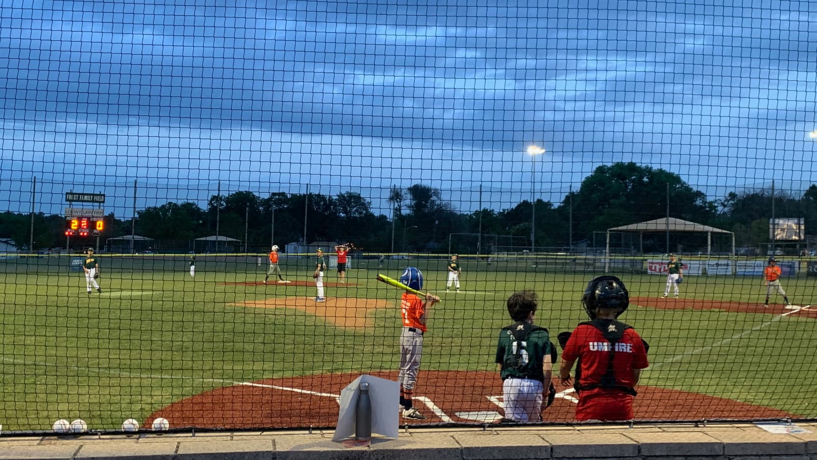 Kids playing baseball under a stormy night sky